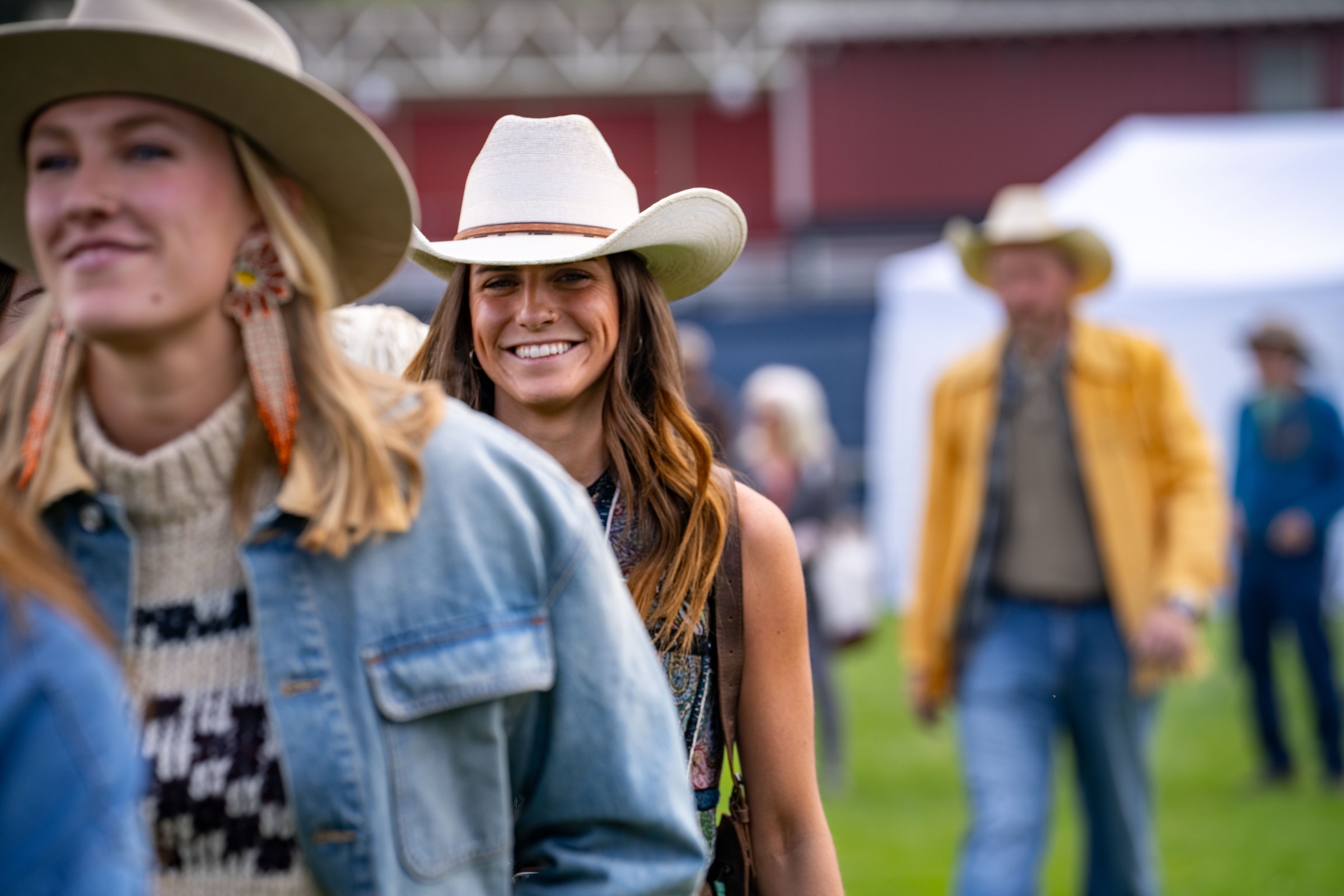 Festival-goers in cowboy hats standing in the grass at Horseshoe, one smiling toward the camera, a red barn and white tents behind them