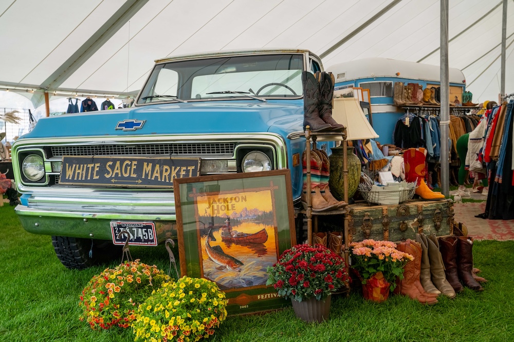 The White Sage Market at Horseshoe: a blue vintage Chevrolet pickup carrying the market's painted sign, with boots, flowers and a framed Jackson Hole print arranged in front of it under the tent